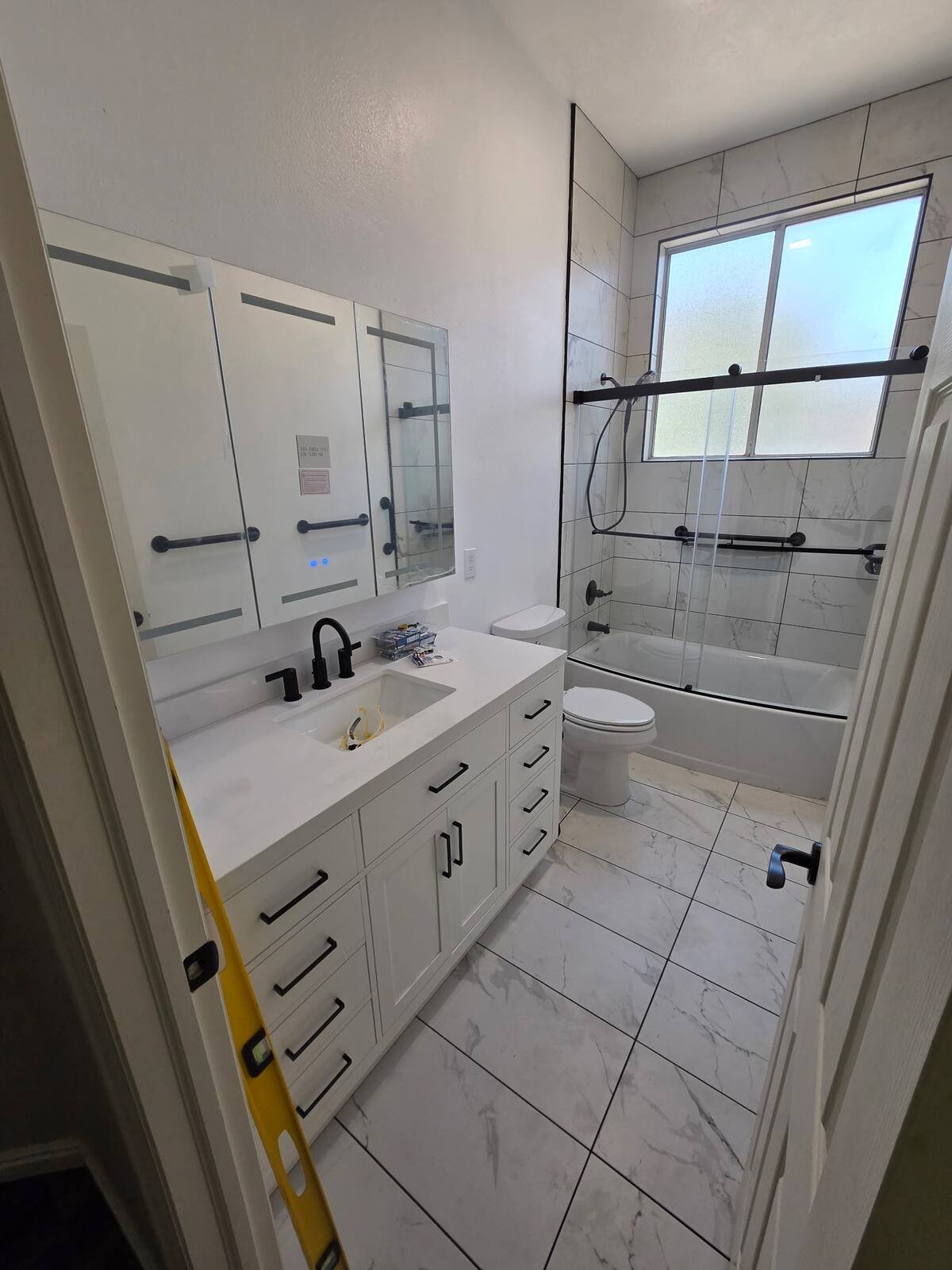 Remodeled bathroom with a white vanity, matte-black faucet, tiled floor and tiled tub surround
