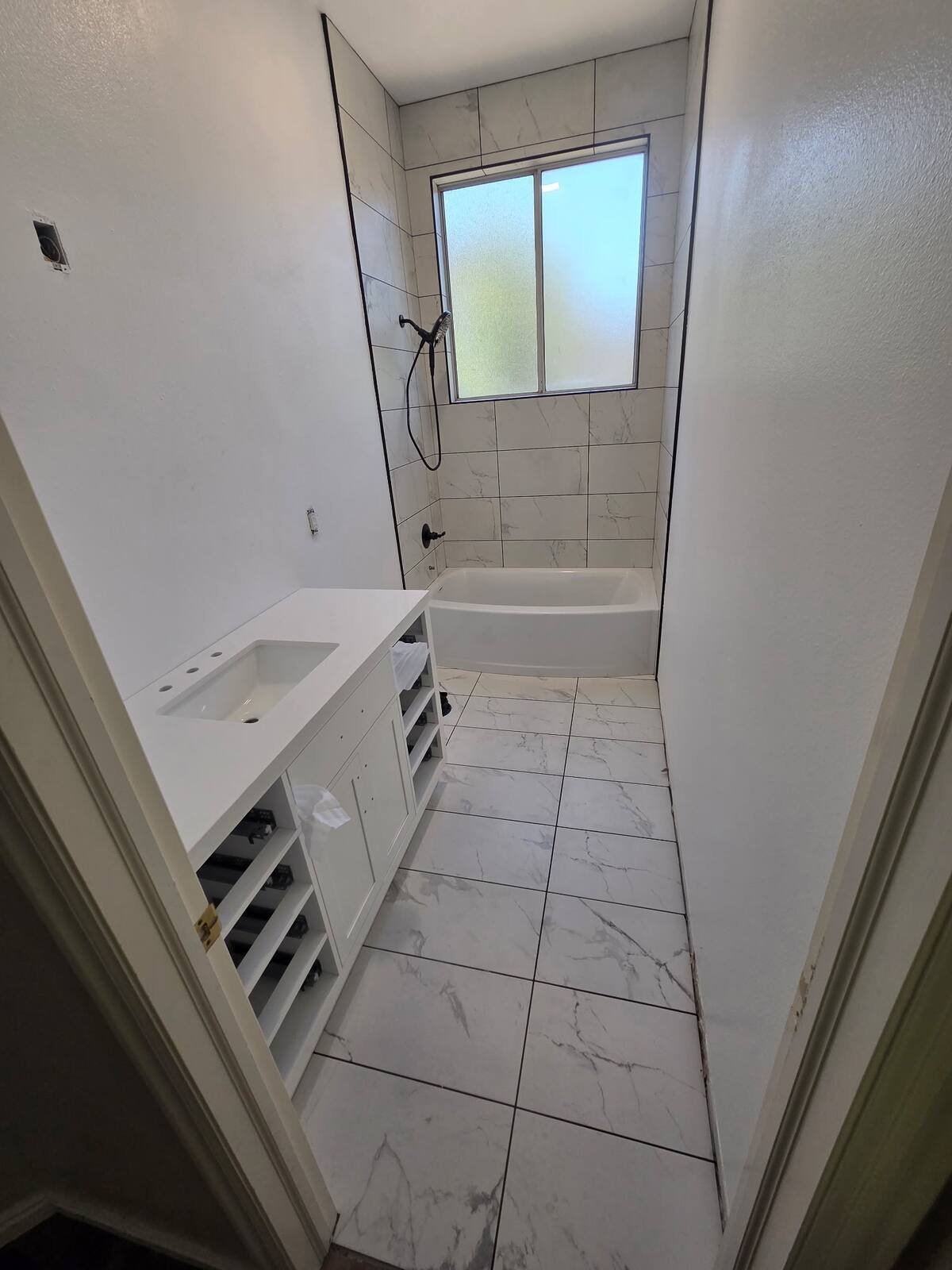 Bathroom remodel in progress with a new white vanity, tiled floor and tub surround