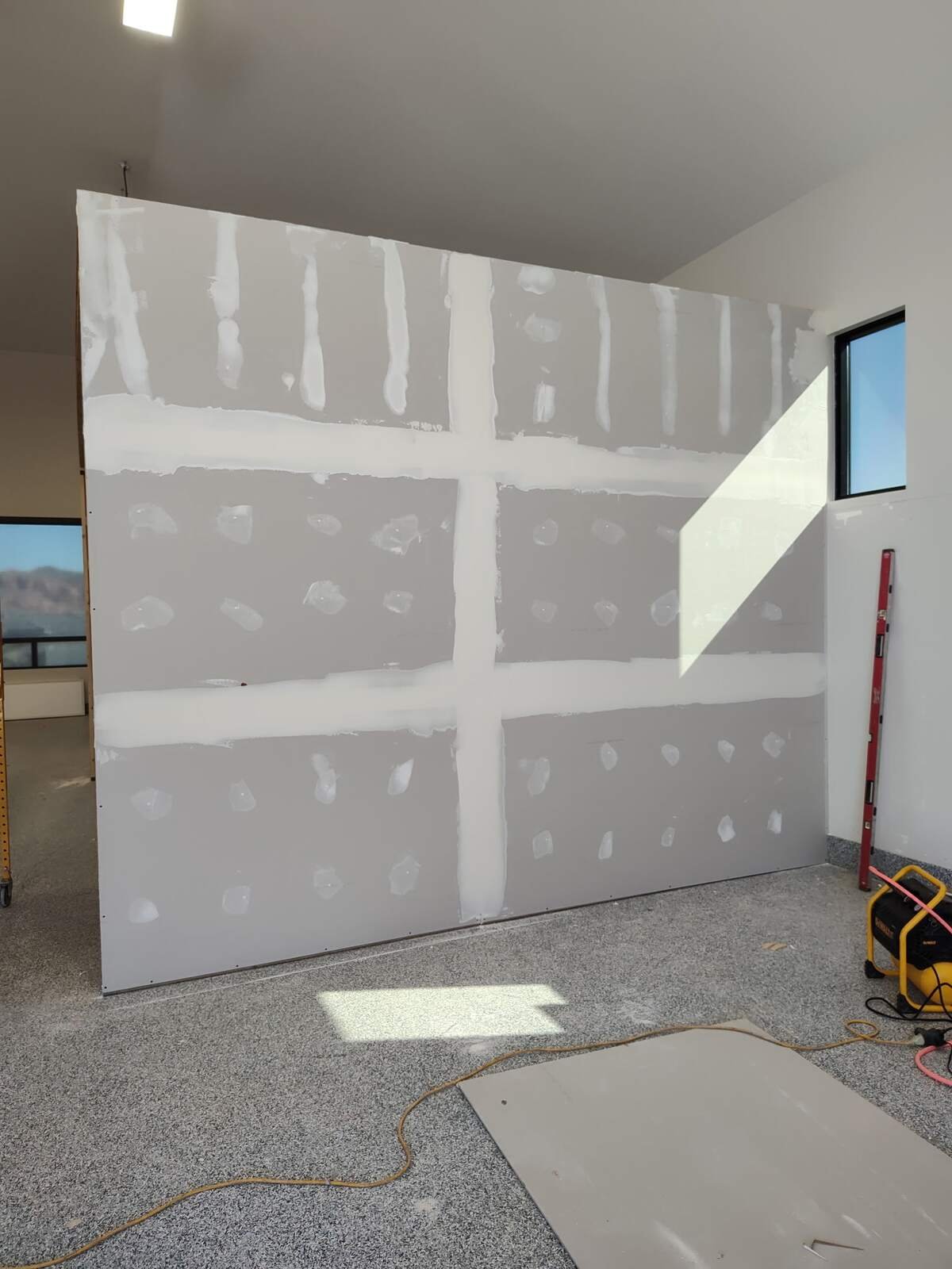 Drywall wall with taped and mudded seams and screw spots, ready for the next coat